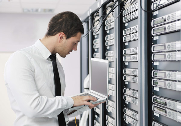 Young man in tie using laptop in network server room