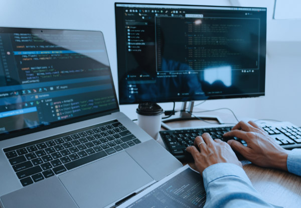 Person using a laptop and a PC at a desk