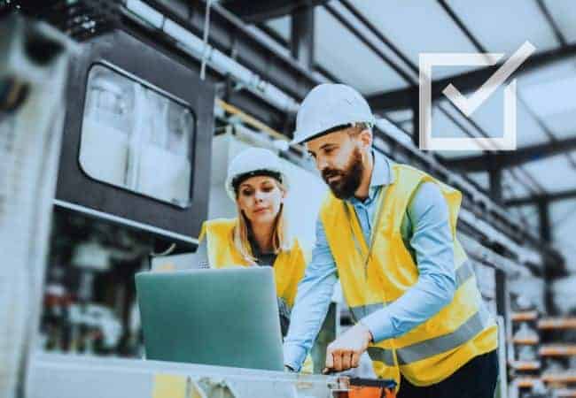 Two people working on a laptop in a factory
