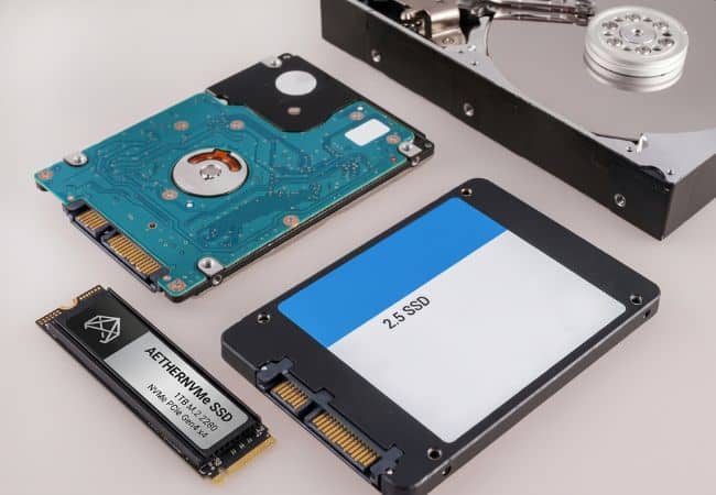 a blue circuit board hard drive, a black ssd module with an m.2 connector, and an open external drive bay showing a 2.5 inch drive slot