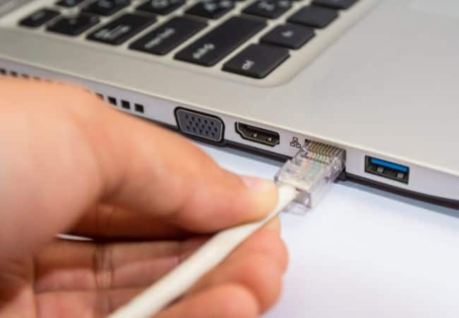 close up of a hand inserting an ethernet cable plug into a laptop’s port