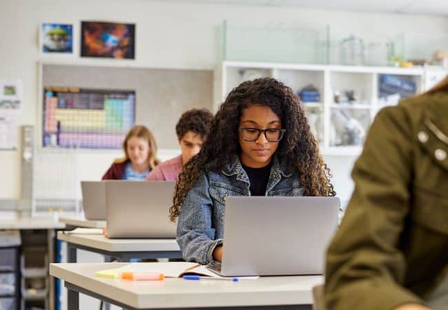 student works at a classroom desk using a laptop